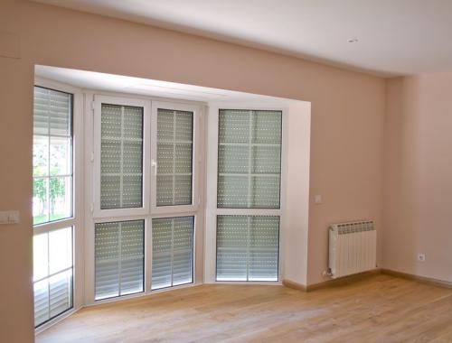 Ventana poligonal de PVC con antepechos fijos y barrotillo en salón.